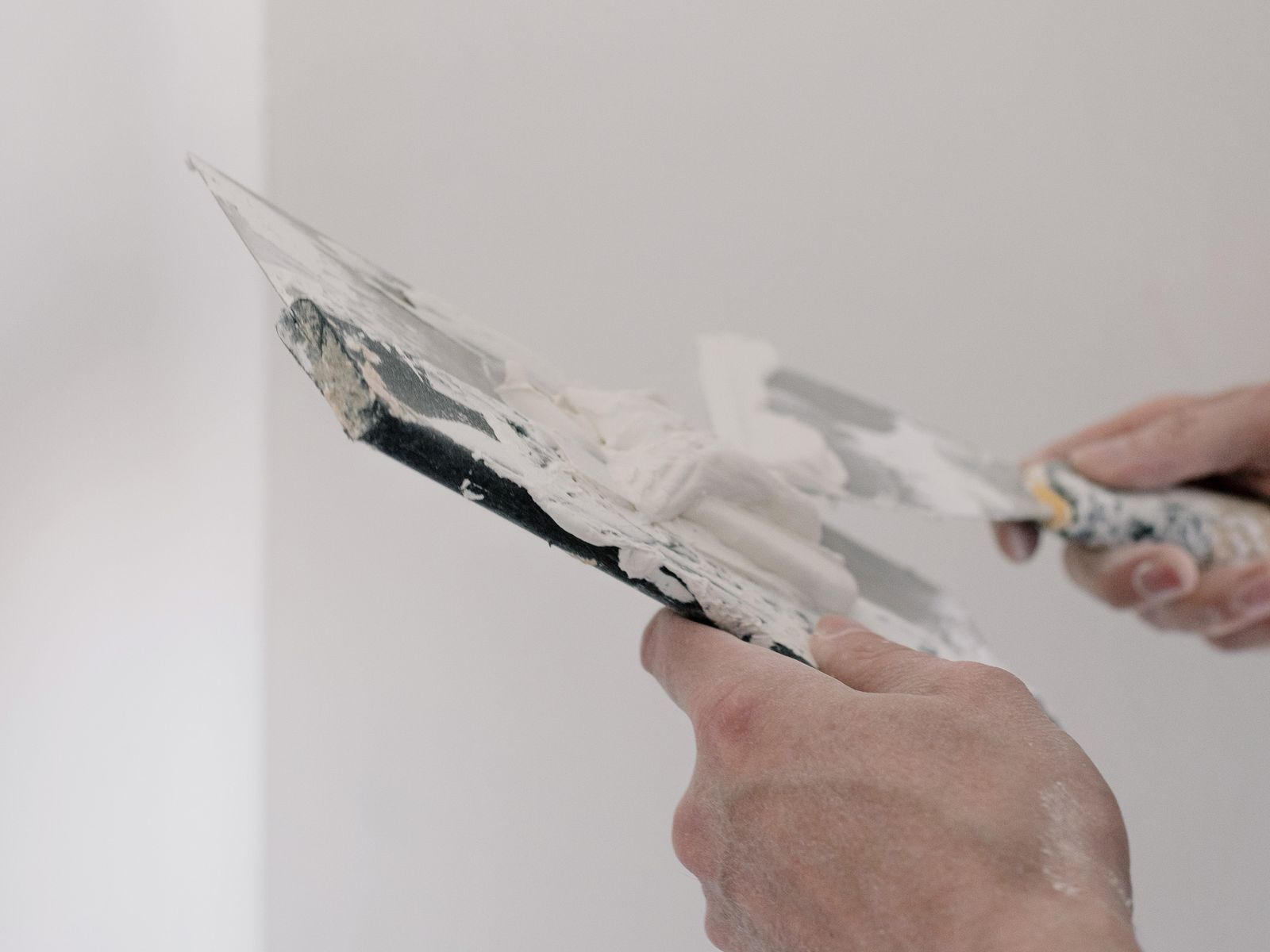 Applying spackle to a nail hole with a metal putty knife on a wall
