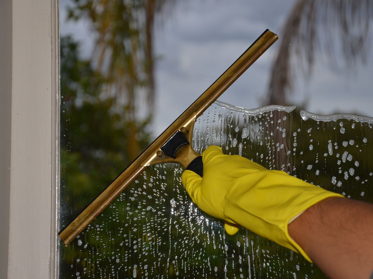 Hand smoothing a wet glass window with a squeegee, the same technique used to apply removable window film