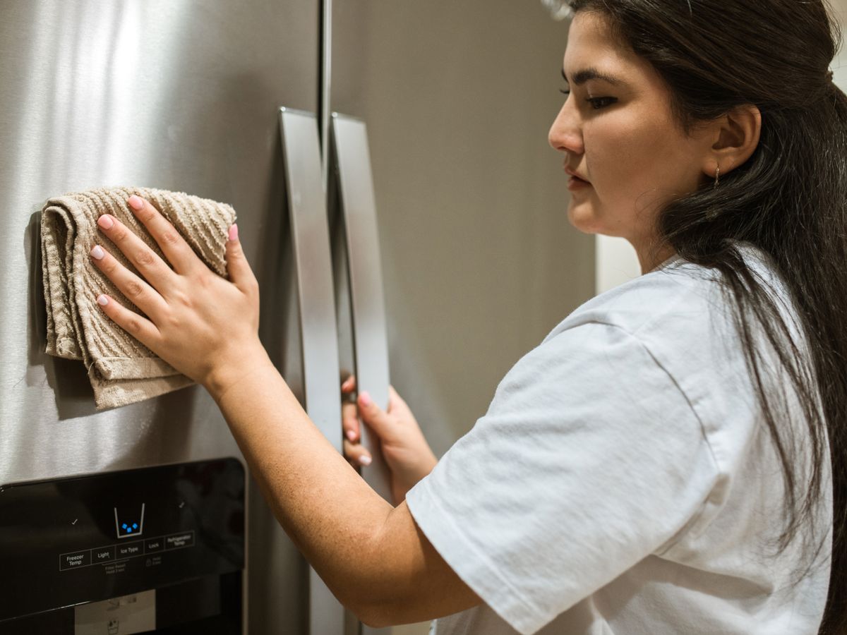 Person wiping down the inside of a refrigerator with a cloth