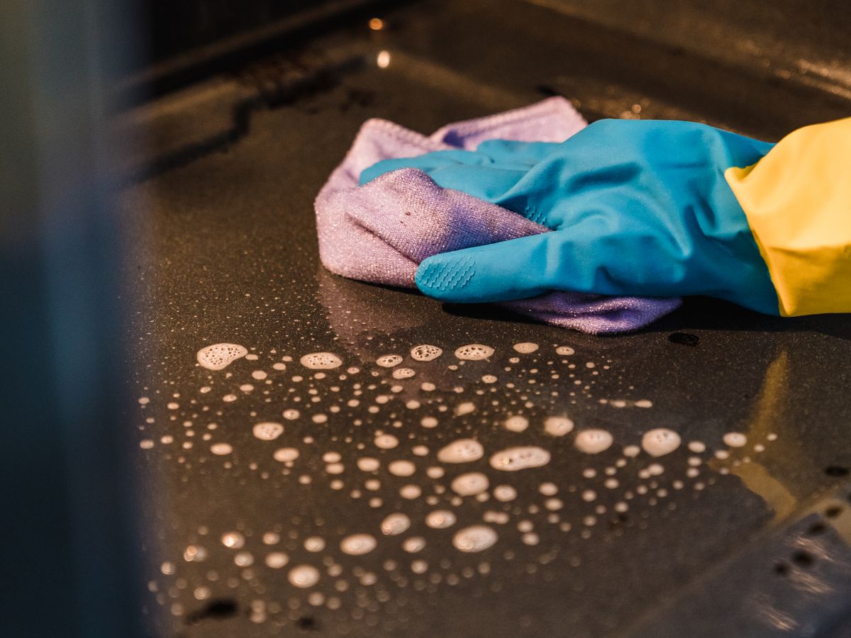 A gloved hand scrubbing to deep-clean a rental oven interior