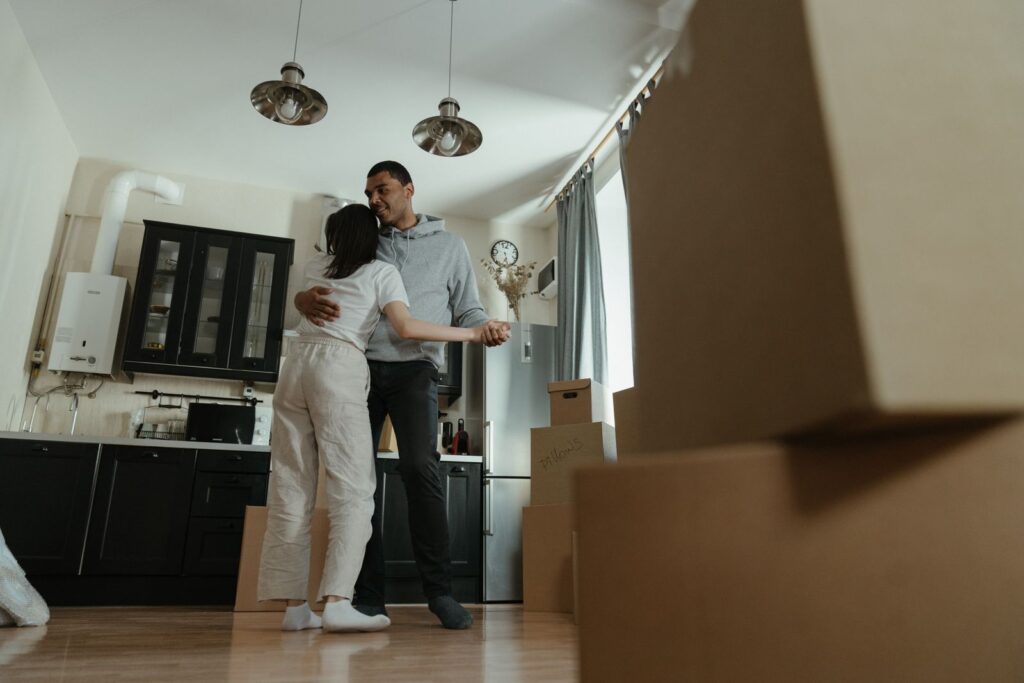 Couple embracing in a new apartment kitchen surrounded by moving boxes on move-in day