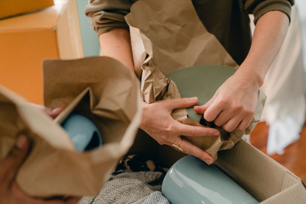 Person wrapping a plate near cardboard boxes using cheap packing materials to move