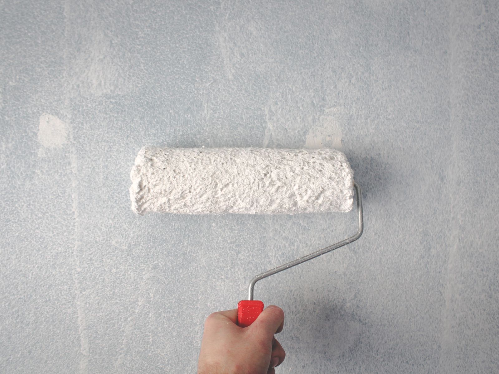 Hand using a roller to touch up paint on a wall as a last-resort fix