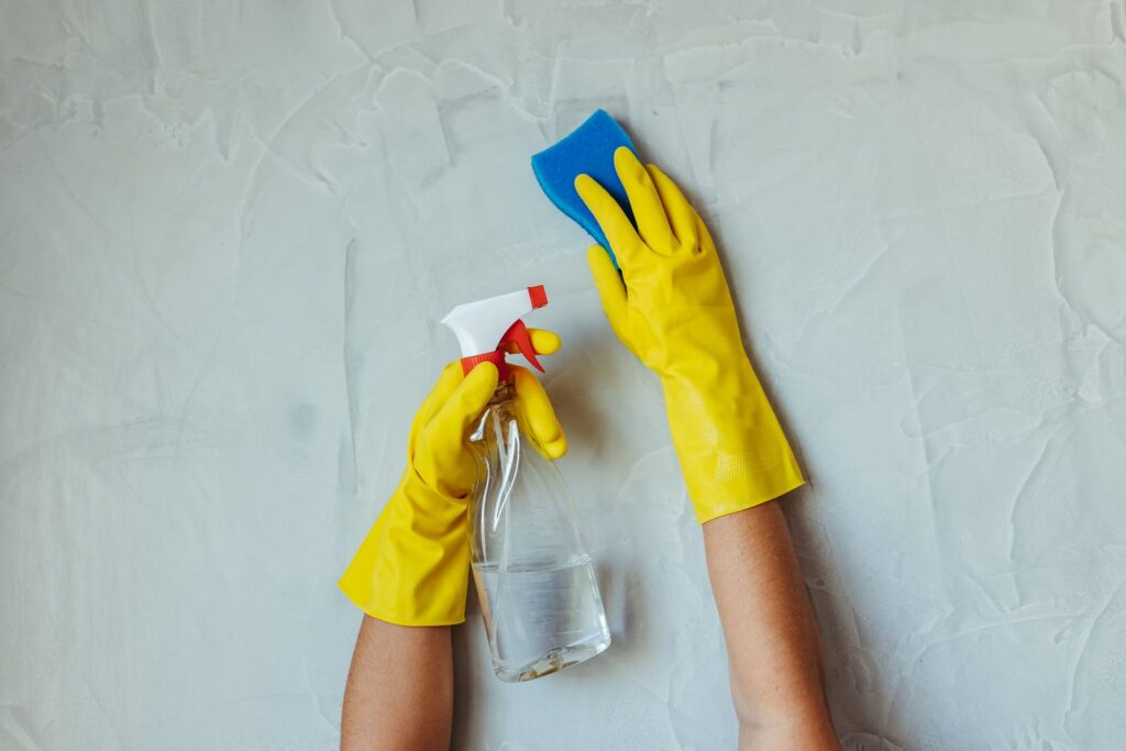 Gloved hands cleaning scuffs and marks from rental walls with a sponge and spray