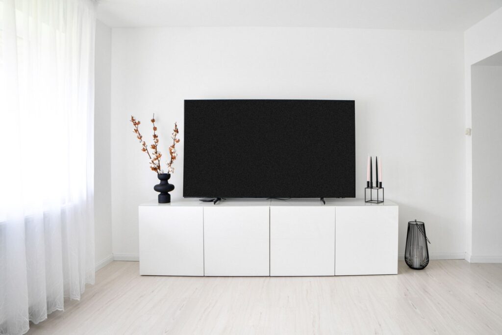 A flat screen TV resting on a white media console in a bright renter-friendly living room, not wall mounted