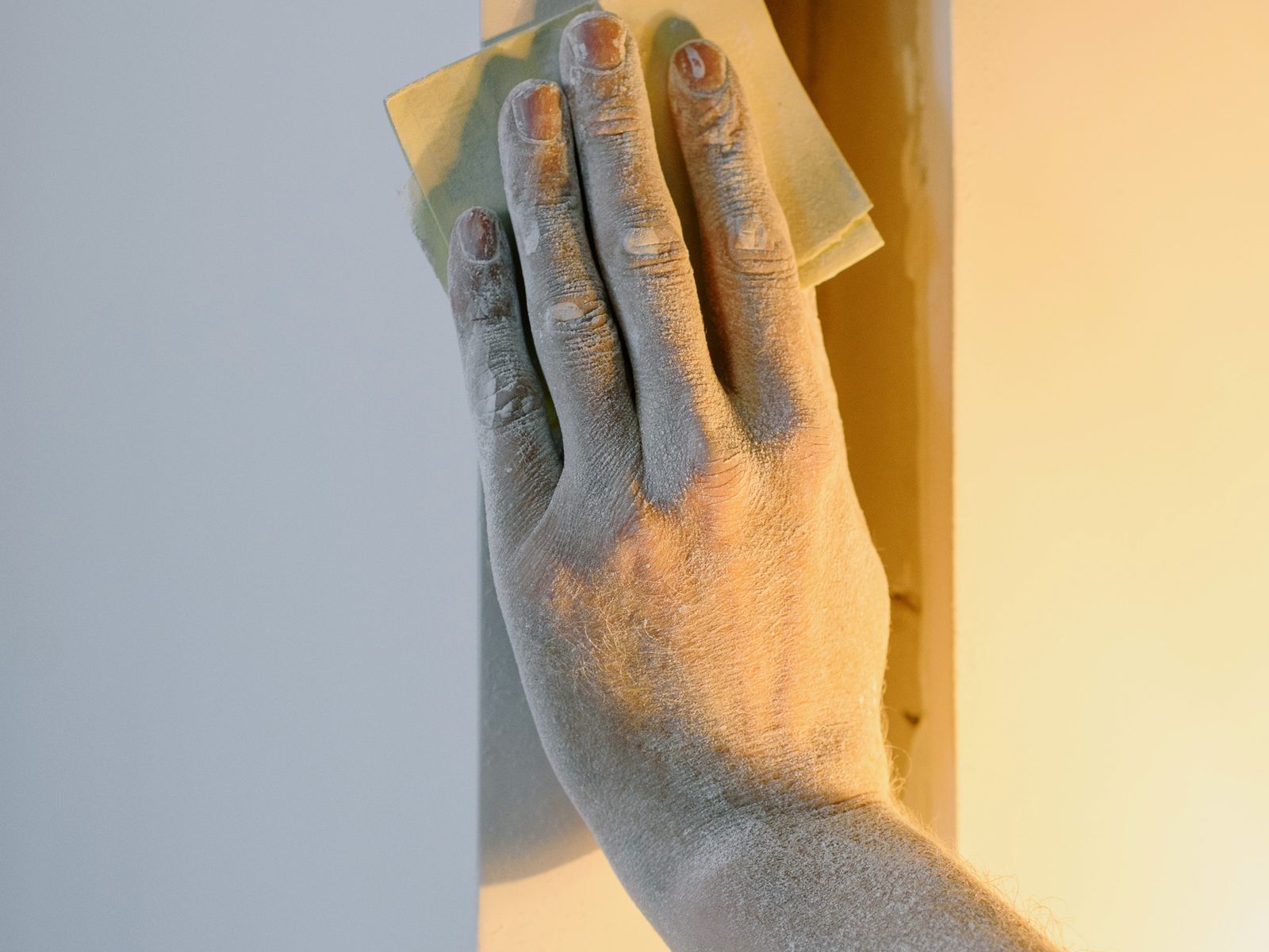 Sanding a filled wall patch smooth with sandpaper before painting