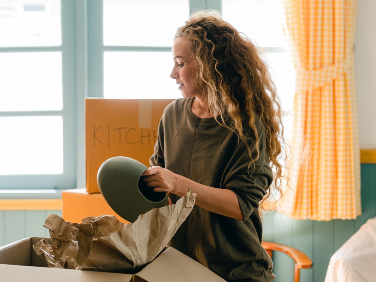 Woman unpacking dishes from a box labeled kitchen, the essentials box for a new rental